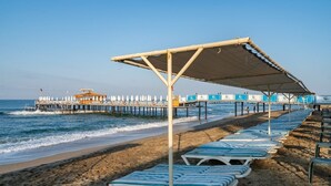 A beach with lounge chairs and umbrellas, a pier with beachside seating, and a lifeguard tower. - Palmeras Beach Hotel (Alanya)