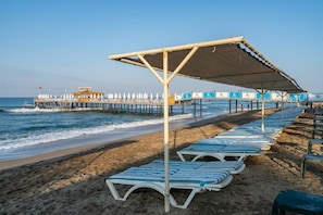 Relax on the beach with comfortable sun loungers and a shaded area under a covered structure.