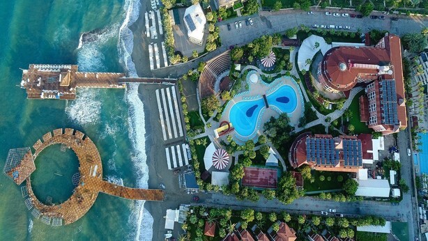 An aerial view of a coastal resort with a swimming pool, a circular water feature, and a pier extending into the sea. - Palmeras Beach Hotel (Alanya)