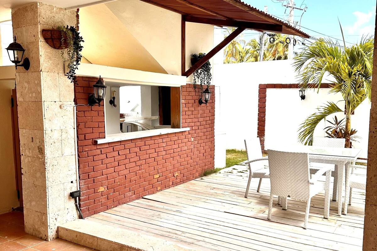 Un patio con pared de ladrillo, una mesa blanca y sillas.