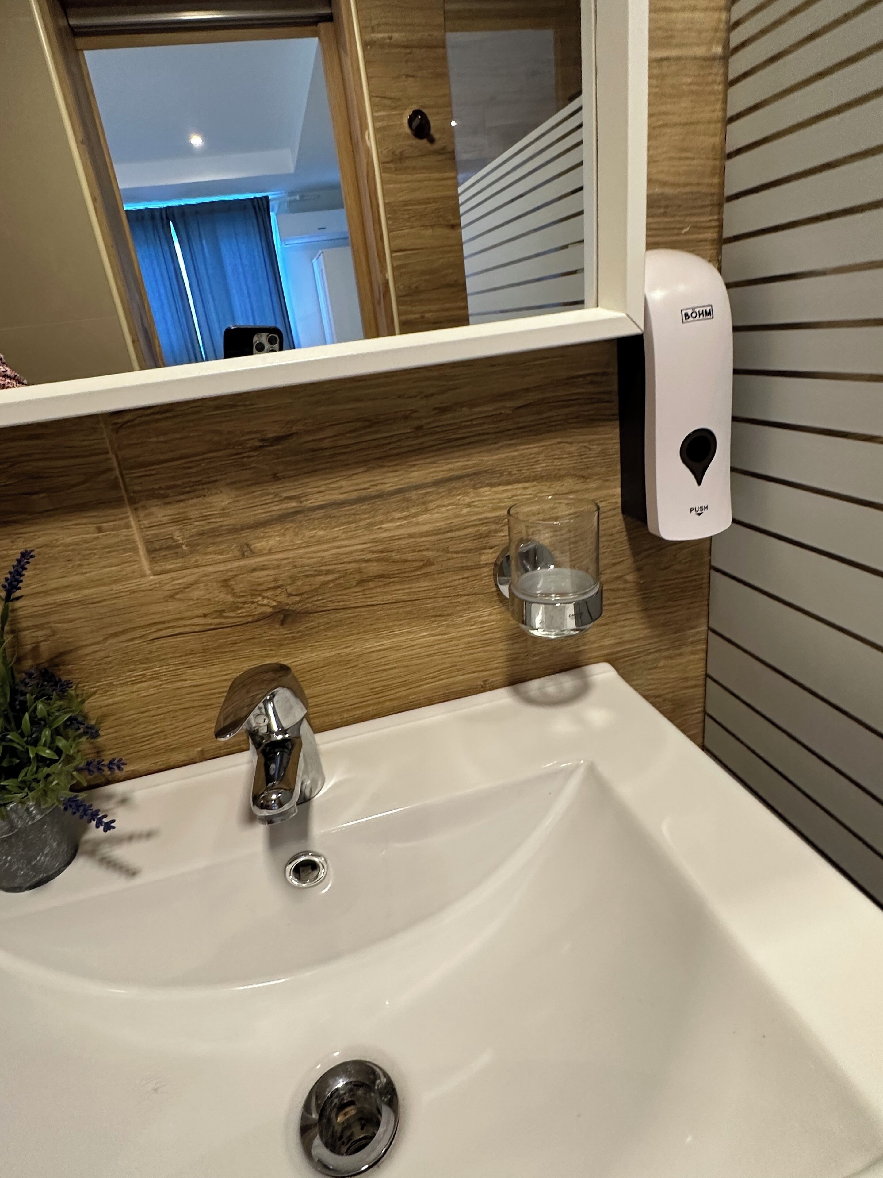A bathroom with a white sink, a mirror, a soap dispenser, and a glass.