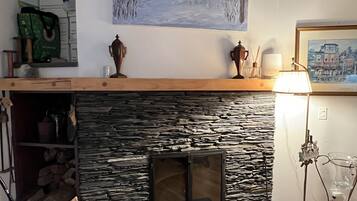 A cozy living room with a stone fireplace, a wooden mantel, and a painting of a snowy landscape.