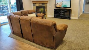 A living room with a brown leather sofa, a fireplace, a television on a stand, and a stone wall. - Cheery and Bright four Bedroom Walkout Basement (Highland)