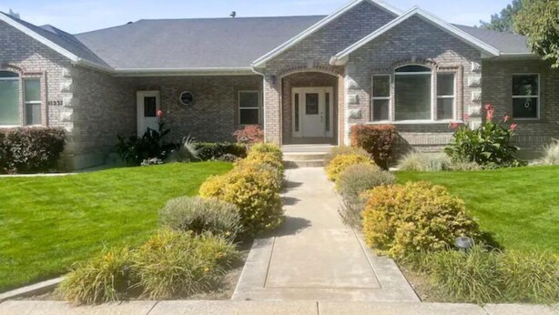 A two-story house with a front entrance, a driveway, and a well-maintained lawn with various shrubs and flowers. - Cheery and Bright four Bedroom Walkout Basement (Highland)