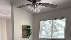 A dining area with a wooden table, white chairs, a ceiling fan, a window with blinds, and a wall-mounted plant. - Sunny Days! Room for everyone and Pet-Friendly! (Pocatello)