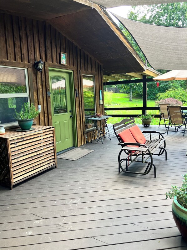 A wooden deck with a green door, a bench with red cushions, and potted plants. - Peaceful and private cabin close to the Little Buffalo River. (Jasper)