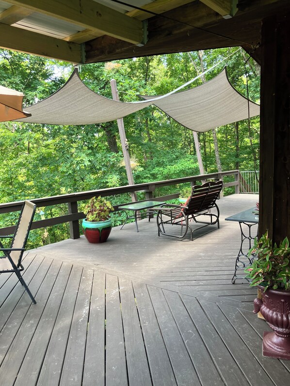 A wooden deck with outdoor furniture, including a table and chairs, surrounded by lush greenery. - Peaceful and private cabin close to the Little Buffalo River. (Jasper)