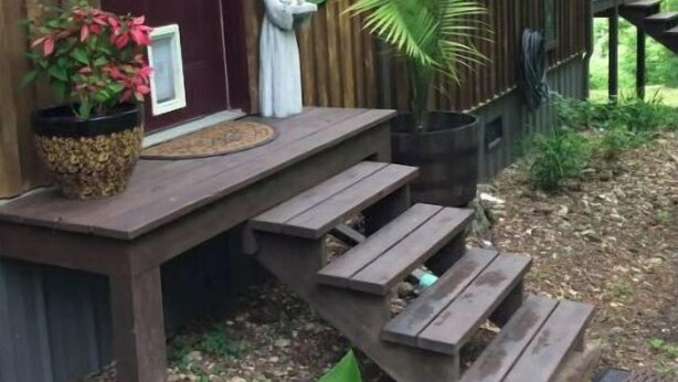A wooden cabin with a porch, a statue, and a potted plant.