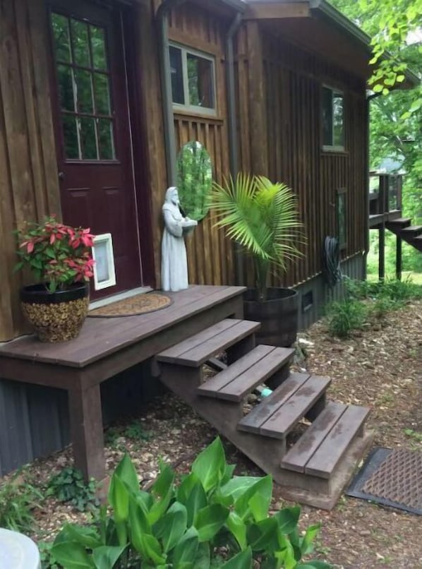 A wooden cabin with a porch, a statue, and a potted plant.