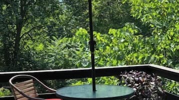 Une terrasse extérieure avec une table ronde et deux chaises, un parasol rouge et une végétation luxuriante en arrière-plan.