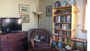 A cozy living room with a wooden ceiling, a bookshelf, a television, a chair, and a small table. - Peaceful and private cabin close to the Little Buffalo River. (Jasper)