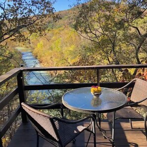 Une terrasse dotée d’une table et de chaises en verre, offrant une vue sur une rivière et les couleurs automnales des arbres.