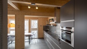 Ett modernt kök med rostfria vitvaror, träbjälkar och en matplats med genomskinliga stolar.