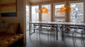 En modern inredning med ett träpanelat tak, stora fönster, ett matbord med genomskinliga stolar och en soffa i läder.