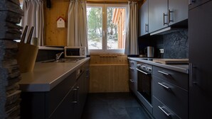 A compact kitchen with dark cabinets, a microwave, a sink, and a window with curtains. - Chalet #7 with IR-sauna (Turrach)