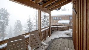 Eine Holzterrasse mit Stühlen, verschneitem Boden und Blick auf ein Gebäude im Hintergrund.