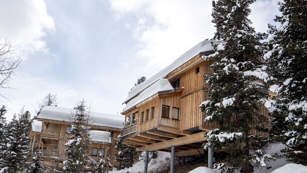 Eine Holzhütte mit Balkon, umgeben von schneebedeckten Bäumen.