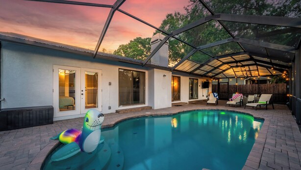 Ein Garten mit Schwimmbad, einer überdachten Terrasse und einem Haus mit Glastüren.