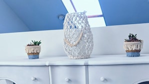 Une pièce avec un bureau blanc, deux paniers en macramé placés en dessous, un tapis blanc moelleux et une lucarne au plafond.