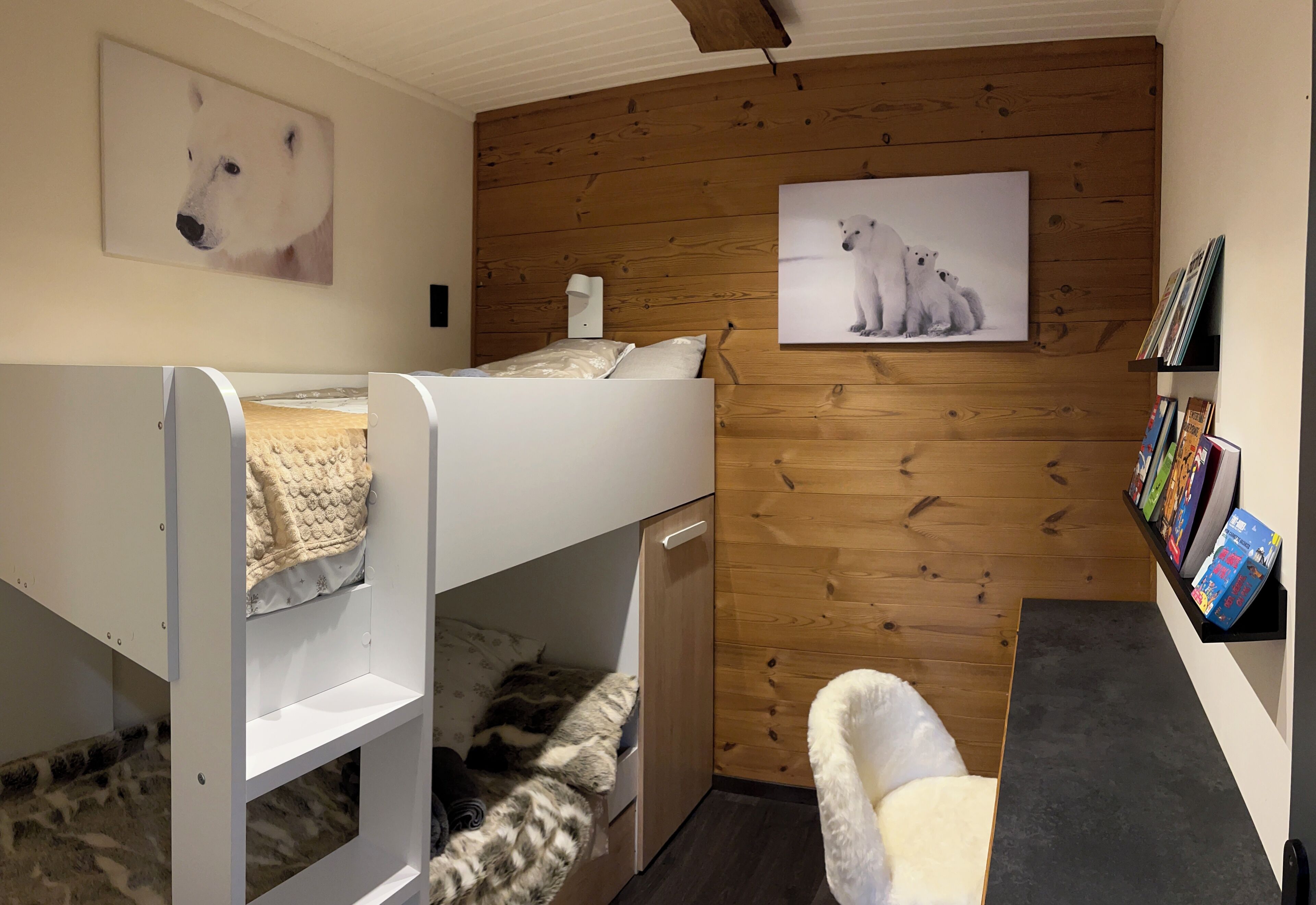 A bunk bed room with a wooden wall, a small desk, and a bookshelf.