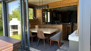 Eine moderne Küche mit Holzausstattung, ein Essbereich mit Tisch und Stühlen sowie ein großes Fenster mit Blick ins Freie.