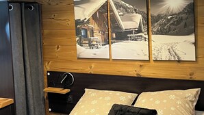 Ein Schlafzimmer mit Holzboden, einem Bett mit gemusterten Kissen, einem Nachttisch und einem Wandbild mit einer verschneiten Berglandschaft.