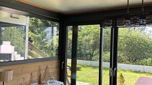 Ein moderner Essbereich mit Holztisch und -stühlen, großen Fenstern mit Blick auf Grünflächen und einer Decke mit hängenden Pflanzen.