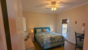 Une chambre à coucher comprenant un lit, des lampes de chevet, une table de nuit en bois, un ventilateur de plafond et une porte donnant sur un espace extérieur.