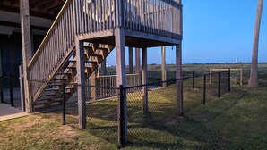 Une structure en bois avec un escalier menant à une zone abritée, le tout entouré d’une clôture en treillis métallique.