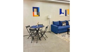 Ein modernes Wohnzimmer mit einem blauen Sofa, einem Esstisch mit Stühlen und abstrakter Wandkunst.