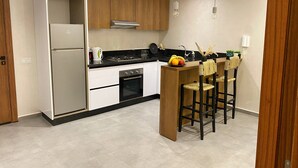 Eine moderne Küche mit integriertem Kühlschrank, Backofen und Gaskochfeld. Holzschränke, eine schwarze Arbeitsplatte und eine kleine Kochinsel mit Barhocker sind vorhanden.