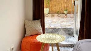 Una stanza con un piccolo tavolo rotondo, una panca imbottita, un cuscino e vista su un patio piastrellato con piante.