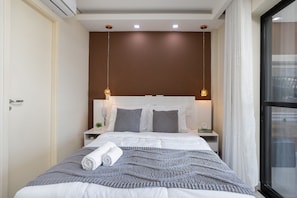 A modern hotel room with a large bed, a nightstand, a wall-mounted air conditioner, and a window with curtains.