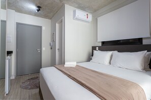 Une chambre d’hôtel comprenant un lit, une table de chevet, une armoire, un appareil de climatisation et une porte.