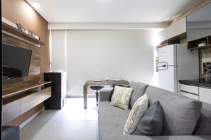 Un salon moderne avec un canapé gris, un téléviseur à écran plat et un coin repas comprenant une table et des chaises.