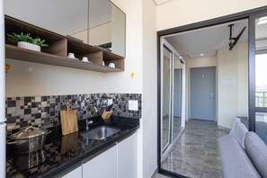A modern kitchen with a black countertop, a sink, and a stove. There is a wooden shelf above the countertop with a potted plant and kitchen items.