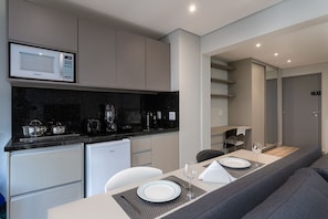 A compact kitchenette with a microwave, stove, and refrigerator. There is a dining area with a table set for two, a sofa, and a mirror.