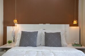 A neatly made bed with white bedding, two gray pillows, a white headboard, and two pendant lights.