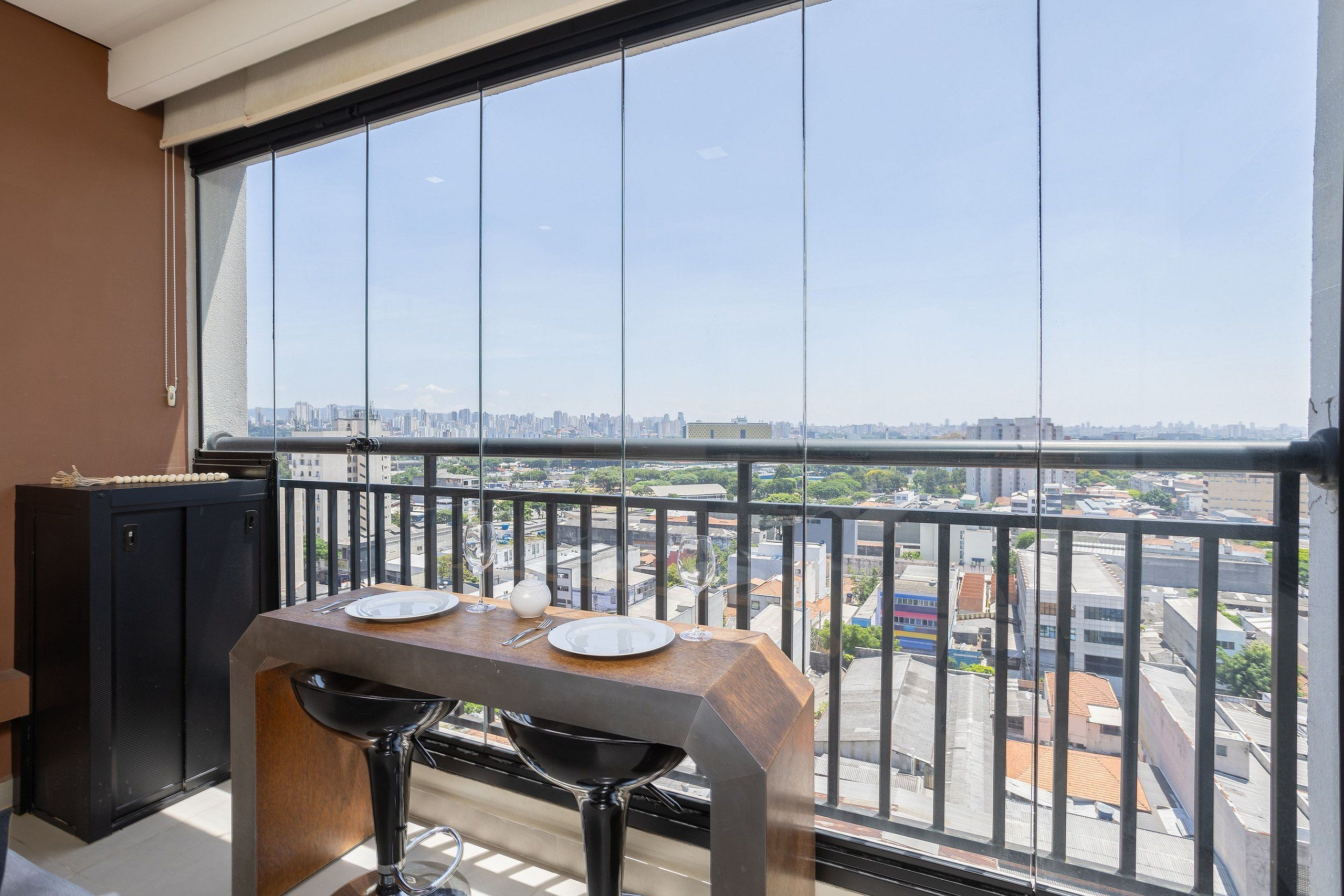 Un balcon avec une table dressée pour deux personnes, un meuble noir et une vue sur la ville.