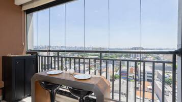 Un balcon avec une table dressée pour deux personnes, un meuble noir et une vue sur la ville.