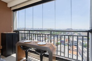 Un balcon avec une table dressée pour deux personnes, un meuble noir et une vue sur la ville.