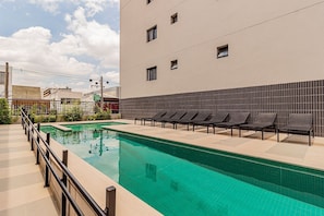 A swimming pool with lounge chairs, a tiled deck, and a building with a tiled facade.