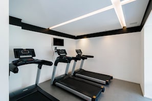 A fitness room with three treadmills, a wall-mounted TV, and a ceiling light fixture.