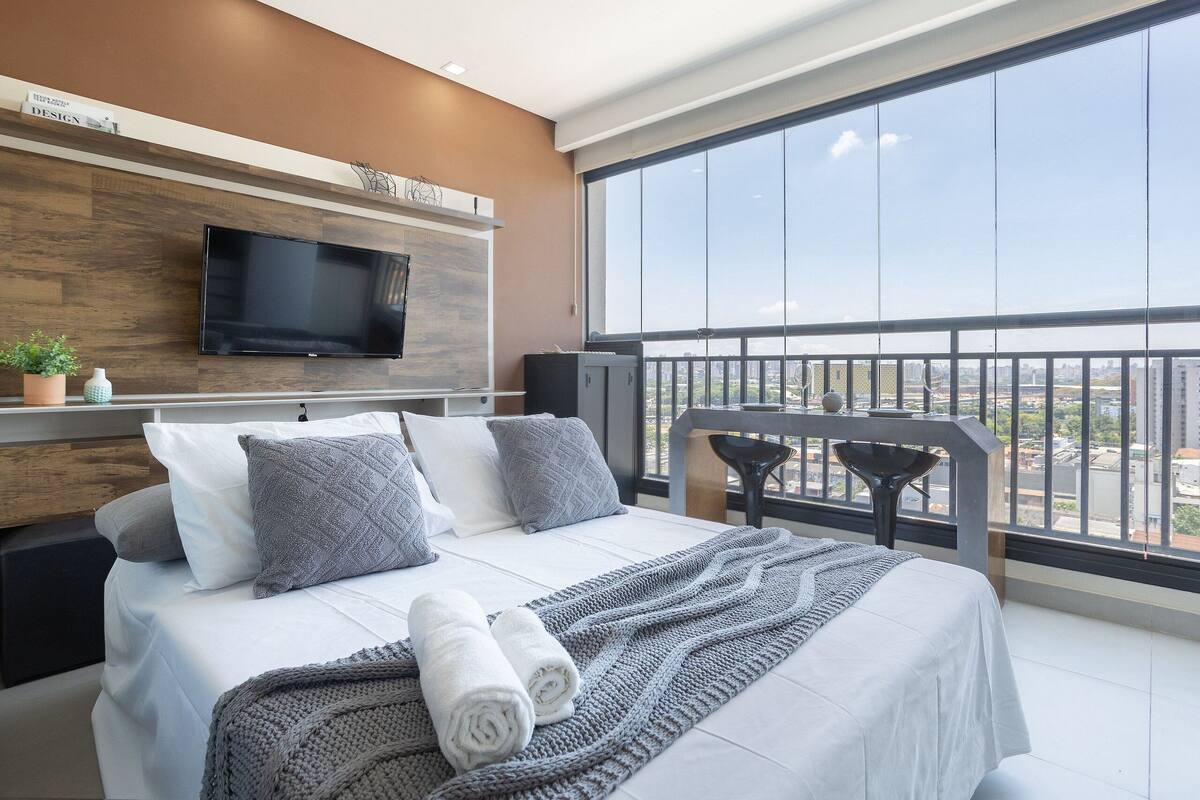 Ein modernes Hotelzimmer mit einem großen Bett, einem Flachbildfernseher, einem Balkon mit Blick und einer Wand mit Holzpaneelen.