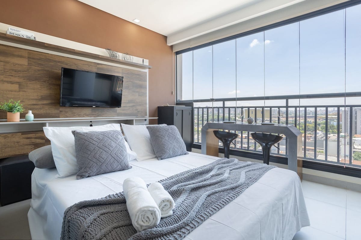A modern hotel room with a large bed, a flat-screen TV, a balcony with a view, and a wooden accent wall.