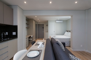 A modern hotel room with a dining area, kitchenette, and a bed.