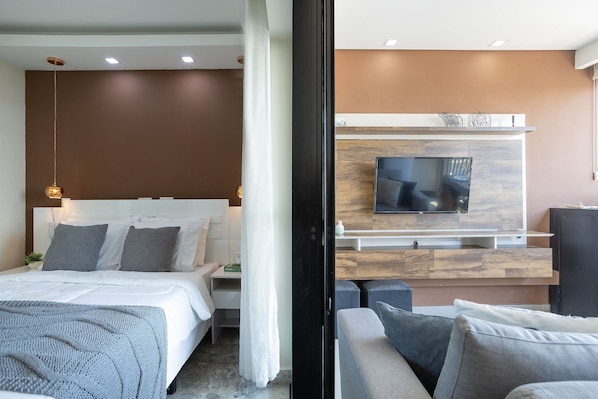 A modern hotel room with a bed, a TV mounted on a wooden wall, a sofa, and a small table.