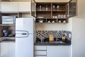 A compact kitchen with a built-in microwave, a refrigerator, a coffee maker, and a tiled backsplash. - Vita Bom Retiro (São Paulo)