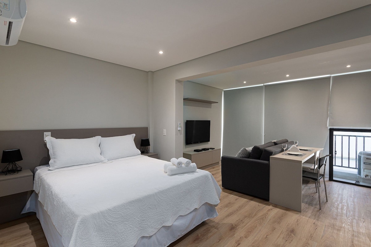 A modern hotel room with a large bed, a desk, a sofa, and a TV.
