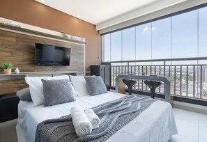 A modern hotel room with a large bed, a flat-screen TV, a balcony with a view, and a wooden accent wall. - Vita Bom Retiro (São Paulo)